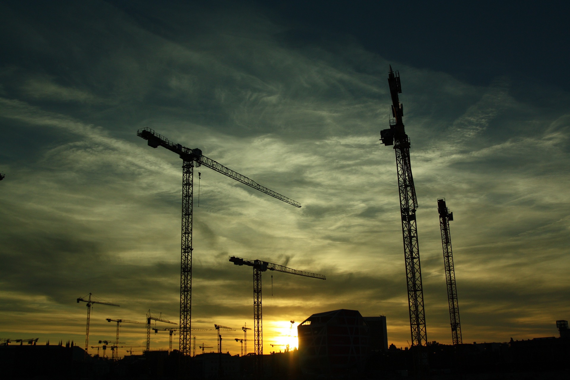 Several construction cranes scattered around a construction site at dusk